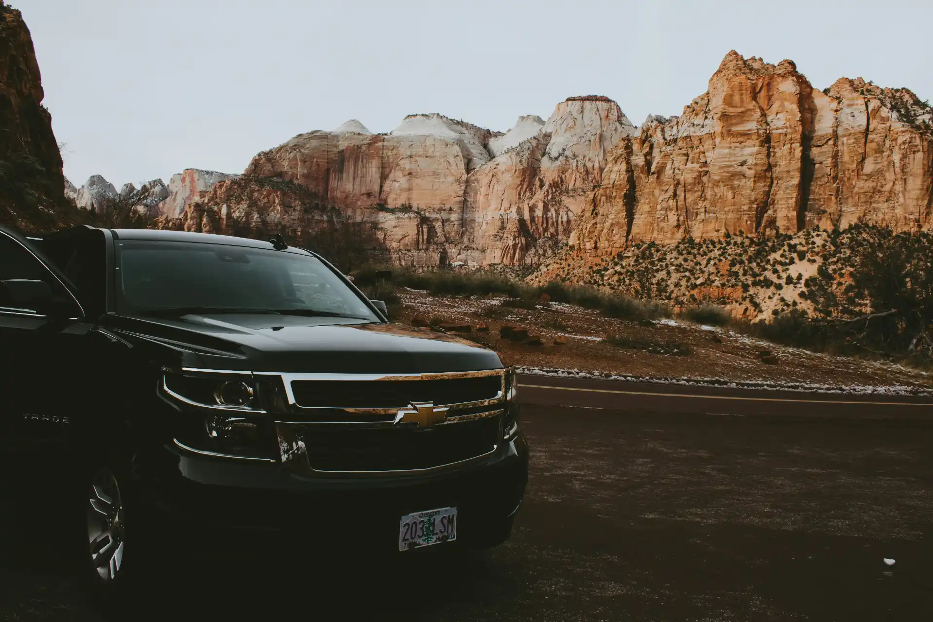 Polished black Cadillac Escalade waiting at an airport curb at dusk, uniformed chauffeur beside the rear passenger door, premium travel photography